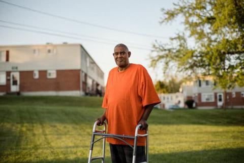 A gentleman wearing an orange shirt standing with a walker outside